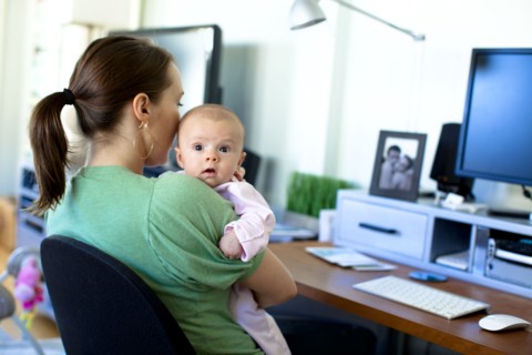 Caucasian mother working in home office and holding baby