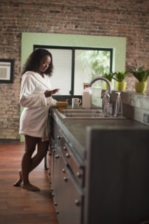 Mixed race woman using cell phone in kitchen