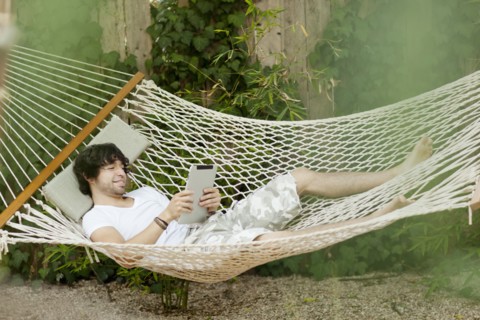 Mixed race man laying in hammock using digital tablet