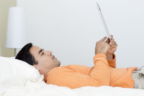 Mixed race man laying in bed using digital tablet