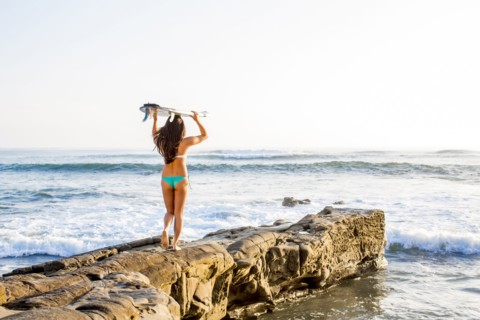 Japanese woman carrying surfboard on beach
