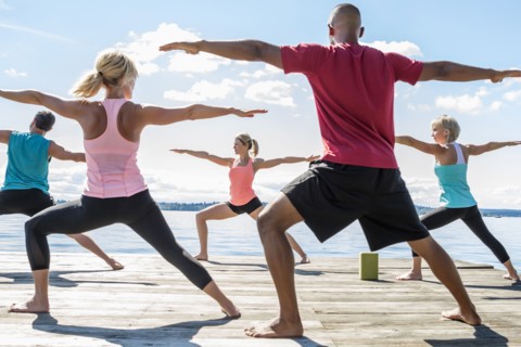 Caucasian people practicing yoga on wooden dock