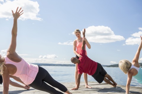 Caucasian people practicing yoga on wooden dock