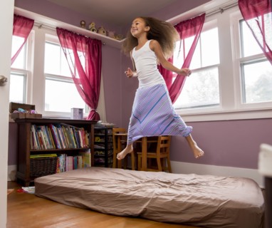 Mixed race girl jumping on bed