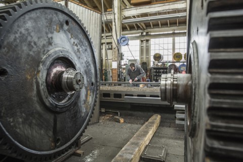 Caucasian man working behind metal cogs in metal shop