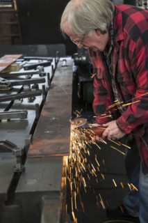 Caucasian man sanding metal in metal shop