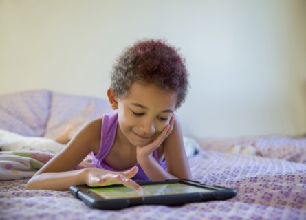 Mixed race girl using digital tablet in bed
