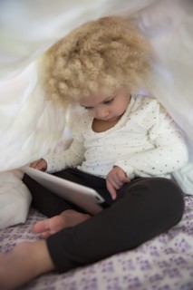 Mixed race girl using digital tablet under covers