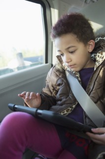 Mixed race girl using digital tablet in back seat of car