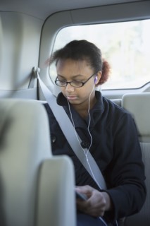Mixed race girl using digital tablet in back seat of car