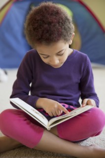 Mixed race girl reading on bedroom floor