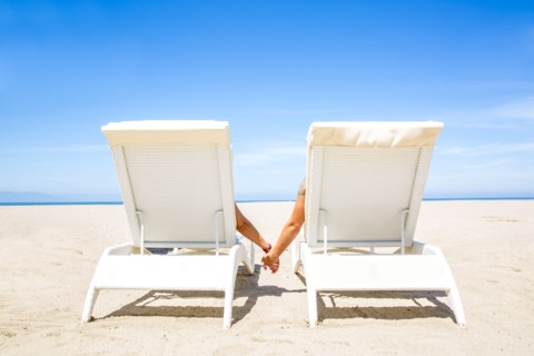Couple holding hands in lounge chairs on beach