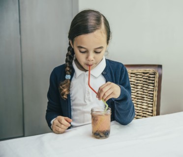 Mixed race girl drinking juice from jar through straw