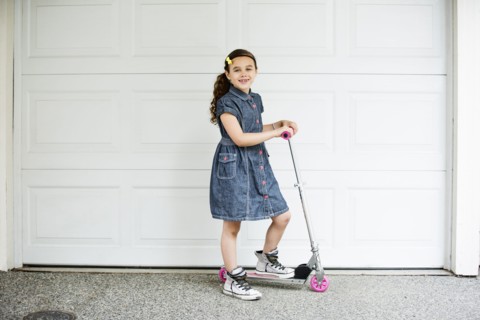 Mixed race girl smiling on scooter in driveway