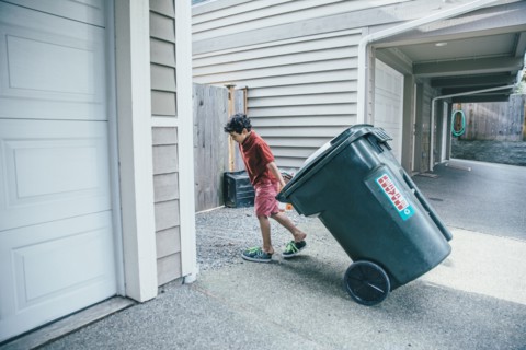 Mixed race boy pulling trash can in driveway