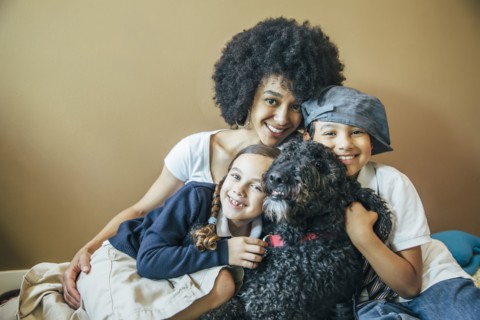 Mixed race mother and children hugging dog