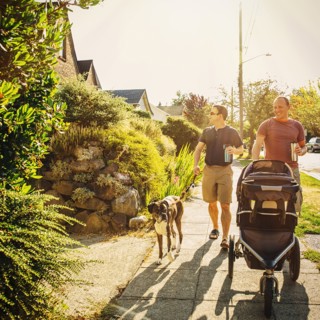 Caucasian gay couple walking dog and pushing stroller on sidewalk