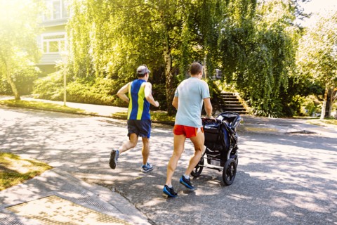 Caucasian gay couple jogging with stroller in neighborhood