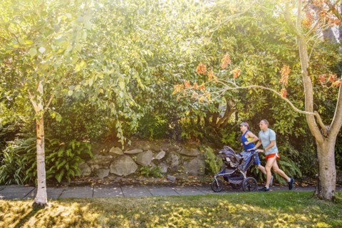 Caucasian gay couple jogging with stroller on sidewalk