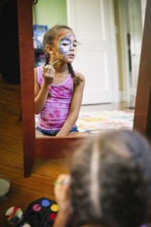 Mixed race girl painting her face in bedroom