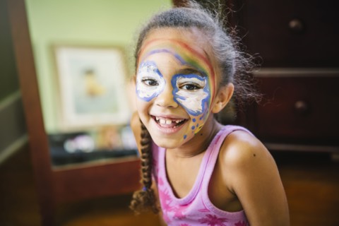Mixed race girl painting her face in bedroom