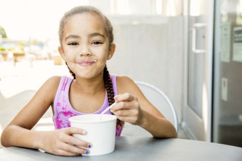 Mixed race girl eating ice cream at outdoor cafe