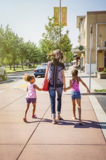 Mother and daughters holding hands on neighborhood sidewalk