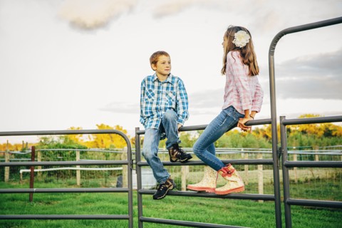 Caucasian children sitting on fence on farm