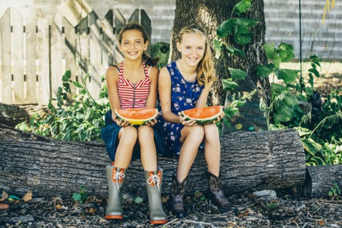 Caucasian girls eating watermelon under tree