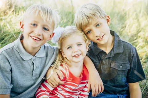 Caucasian brothers and sister smiling in grass