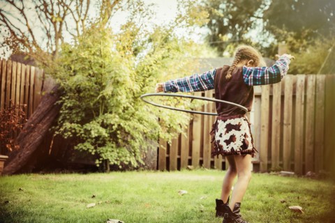 Mixed race girl in cowboy costume spinning plastic hoop in backyard