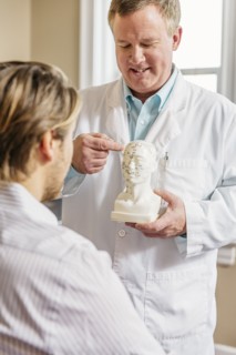 Caucasian acupuncturist showing patient carved bust with diagram