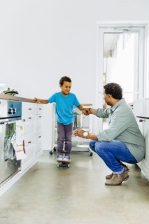 Father helping son balance on skateboard in kitchen
