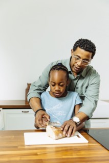 Father teaching daughter to slice bread in kitchen