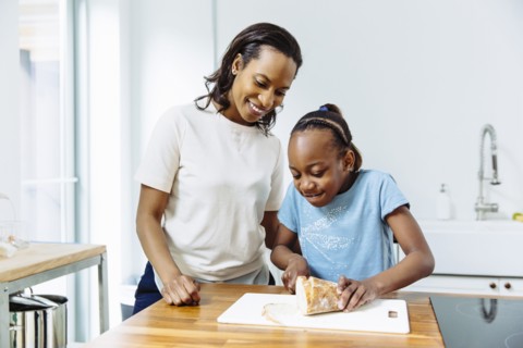 Black mother and daughter slicing bread in kitchen