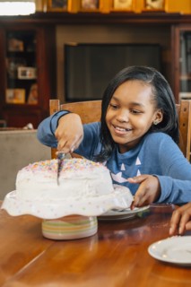 Black girl cutting cake at birthday party