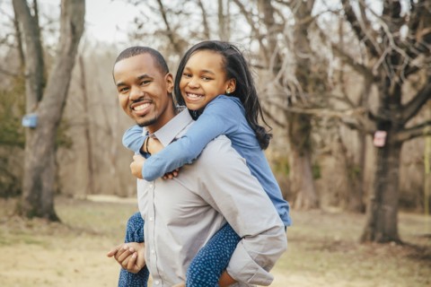 Black father carrying daughter piggyback outdoors