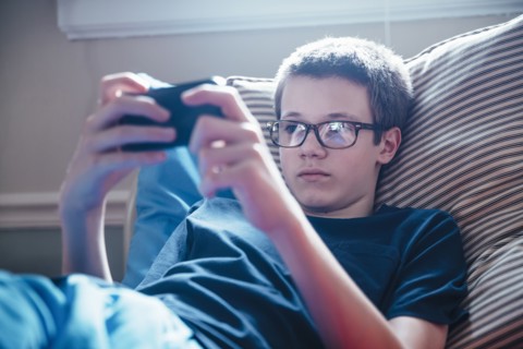 Caucasian boy using cell phone on bed