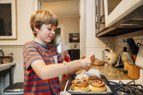 Caucasian boy frosting cinnamon rolls in kitchen