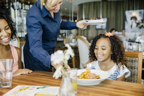 Server bringing birthday dessert to girl in restaurant