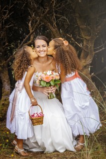 Flower girls kissing bride outdoors