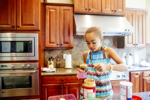 Mixed race girl scooping peanut butter in kitchen