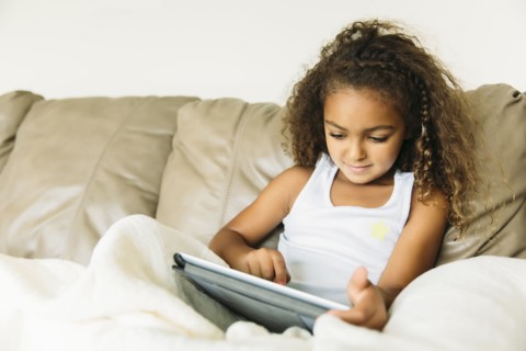 Mixed race girl using digital tablet on sofa