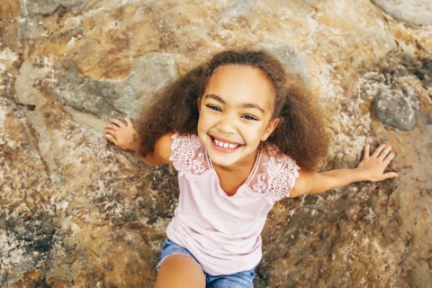 Mixed race girl smiling on rock outdoors