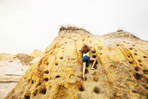 Mixed race girl climbing cliff rock