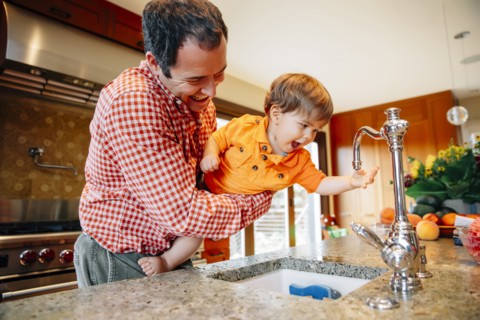 Father and son playing with faucet in kitchen