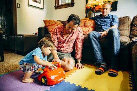 Gay fathers playing with baby son in living room