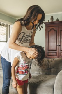 Mother styling hair for daughter in living room
