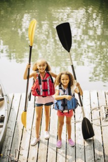 Mixed race sisters holding oars at lake