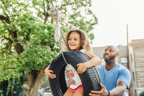 Father pushing daughter on tire swing